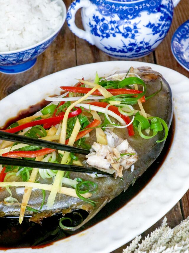 Steamed pompano fish Chinese- style in a serving platter with sliced ginger, green onions, and cilantro on top.