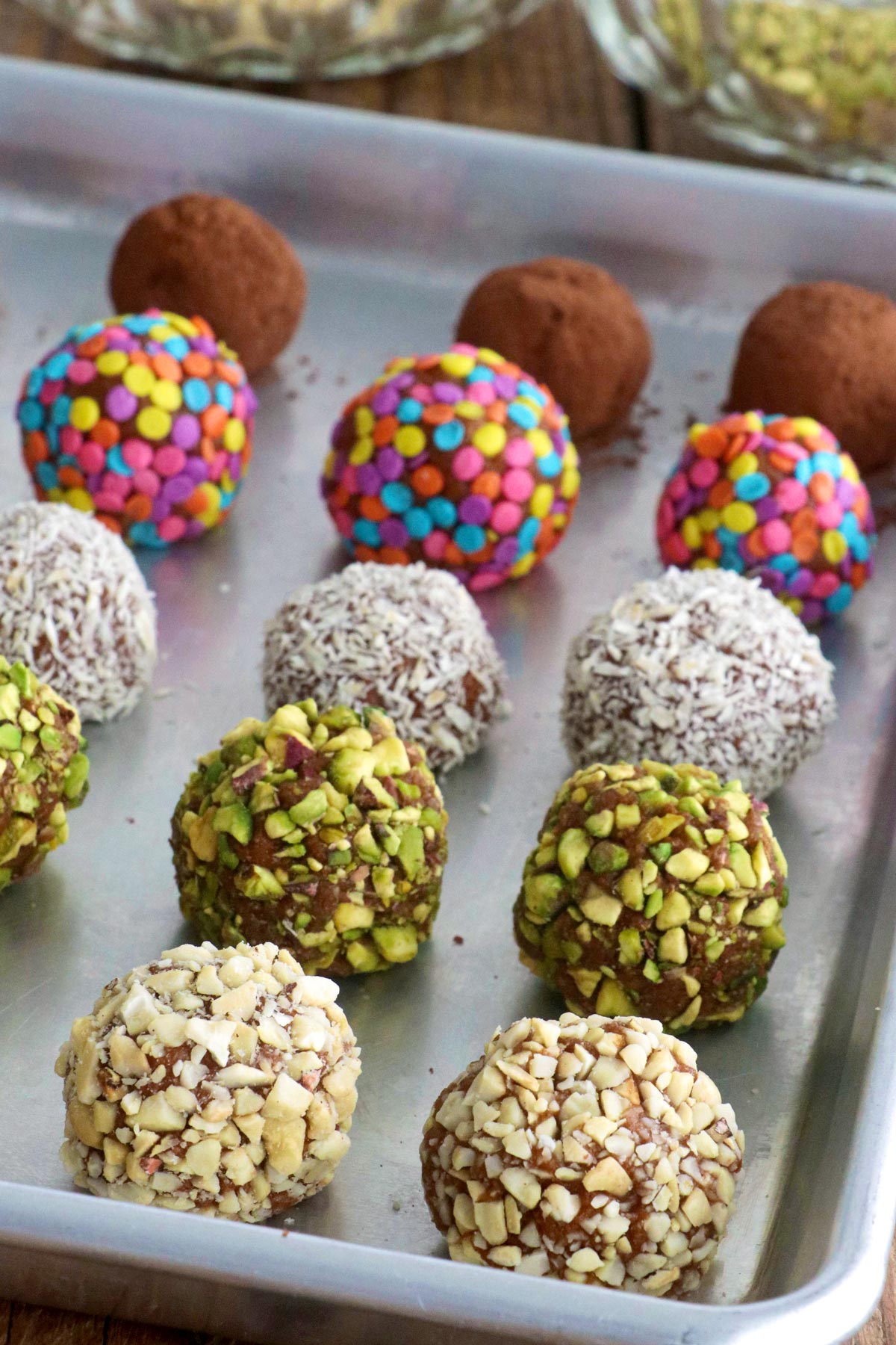 Graham balls on a baking sheet with ground cashew, ground pistachio, desiccated coconut, candy sprinkles, and cocoa powder coatings.