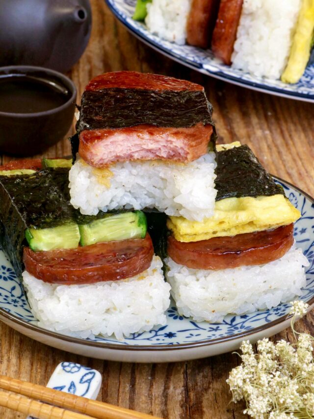 Variety of Spam Musubi with luncheon meat, cucumber, an egg roll on a serving plate.