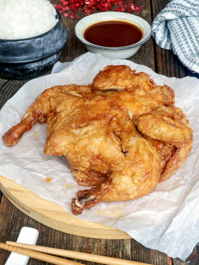 Super crispy whole fried chicken on a serving plate served with dipping sauce and rice.